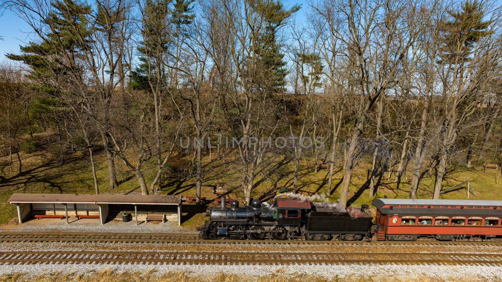 A Drone View of a Restored Steam Passenger Train Traveling Thru Farmlands Pulling Up to a Small Station on an Autumn Day