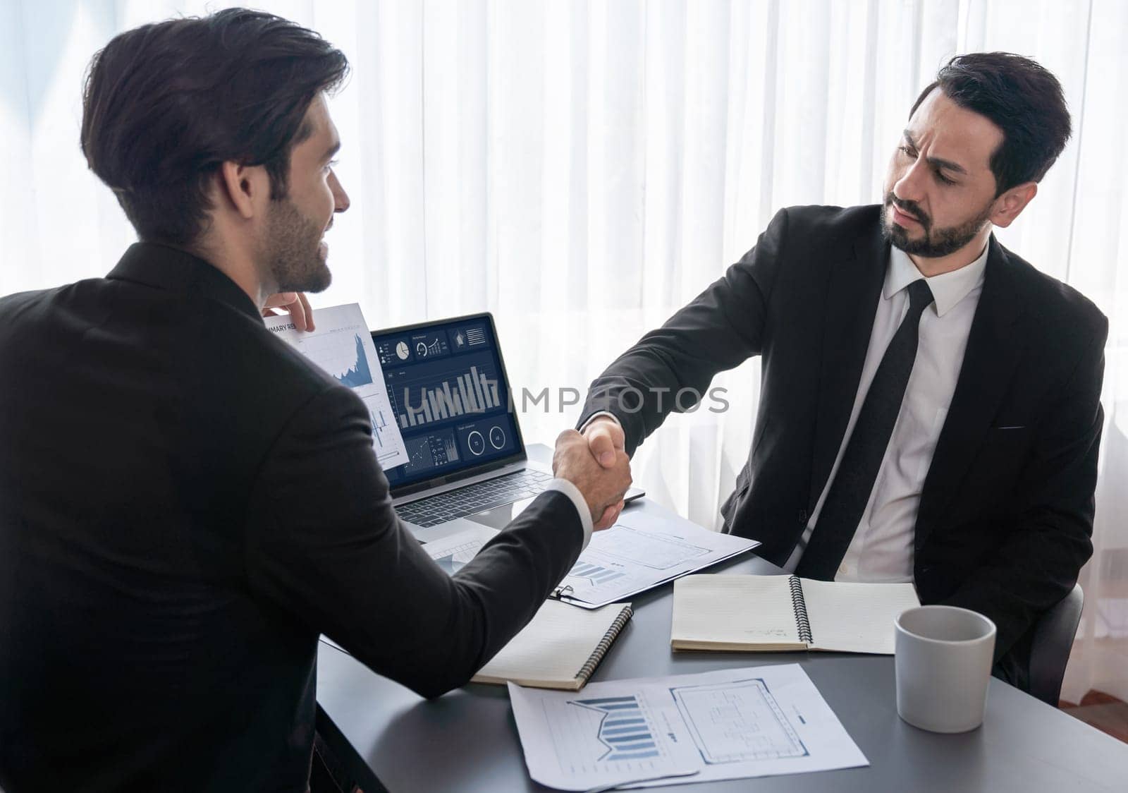 Business partnership meeting with successful trade agreement with handshake or greeting in corporate office desk. Businessman in black suit shaking hand after finalized business deal. Fervent