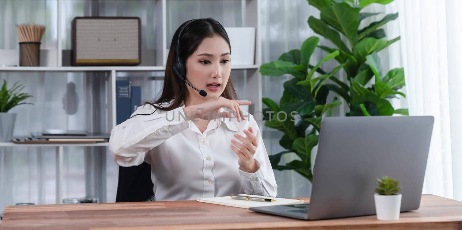 Enthusiastic asian call center with headset and microphone working on her laptop by biancoblue