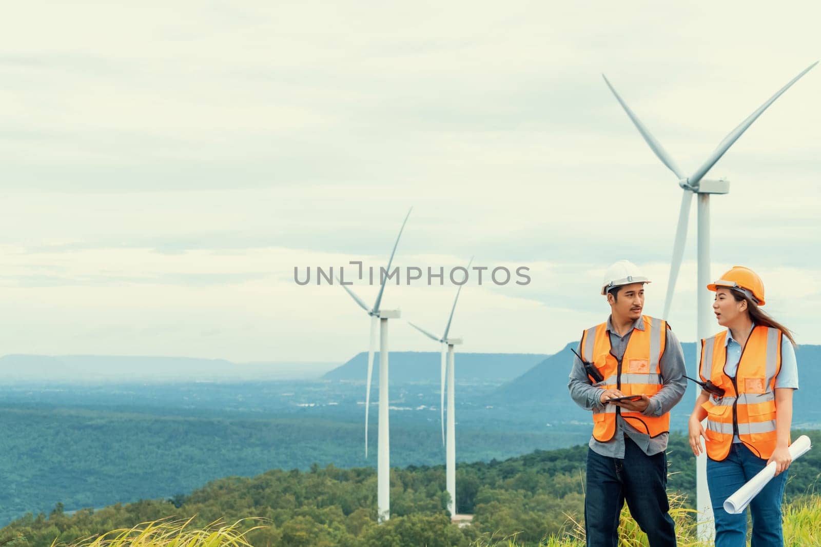 Male and female engineers working on a wind farm atop a hill or mountain in the rural. Progressive ideal for the future production of renewable, sustainable energy.