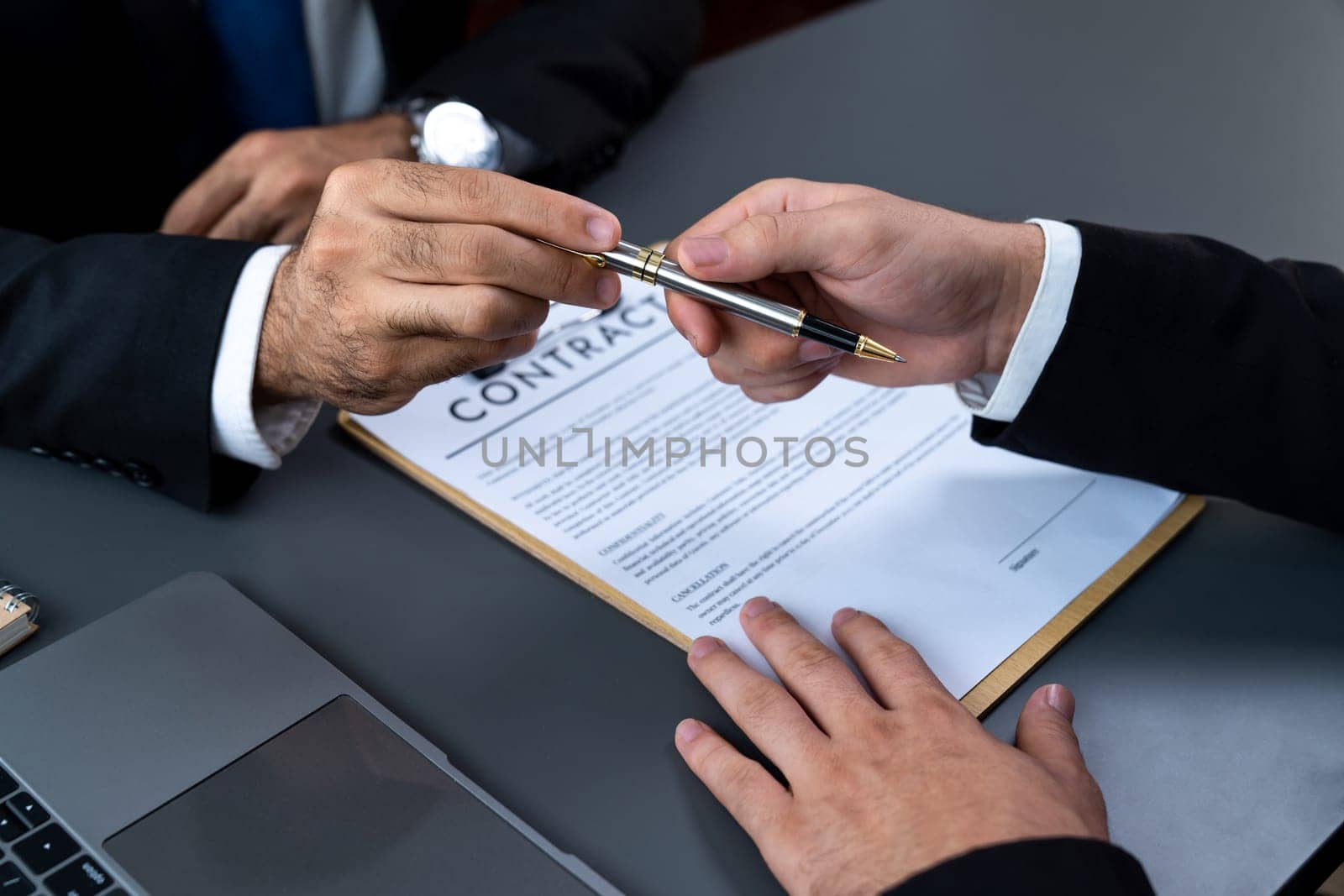 Two businesspeople sit across the desk as business deal is taking place. Corporate attorney giving a pen for client or partner to sign contract paper, sealing the deal with signature. Fervent