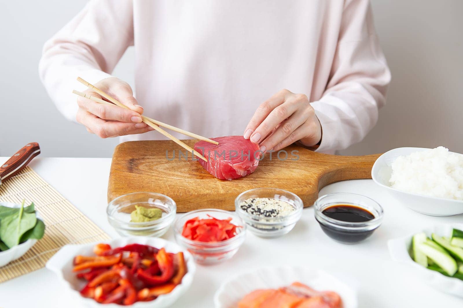 The process of preparing sushi, preparing all the ingredients for sushi, the girl is holding tuna with chopsticks