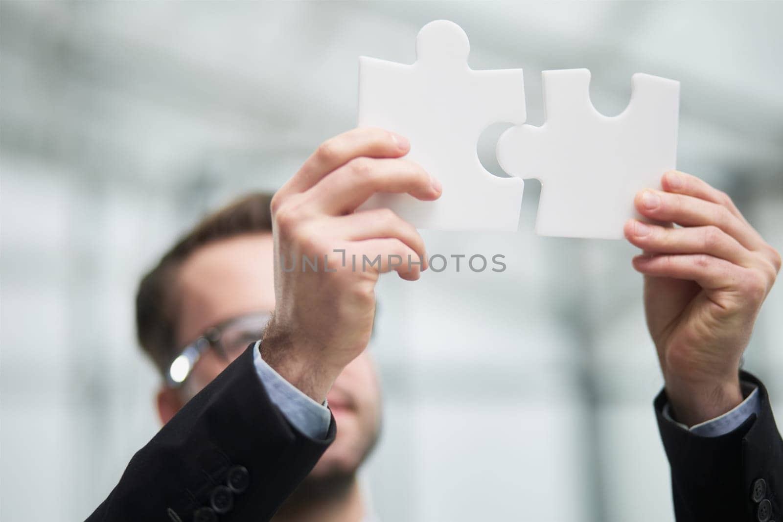 Portrait of an optimistic businessman holding puzzle pieces, solving problems, looking at the camera, wearing a black suit.