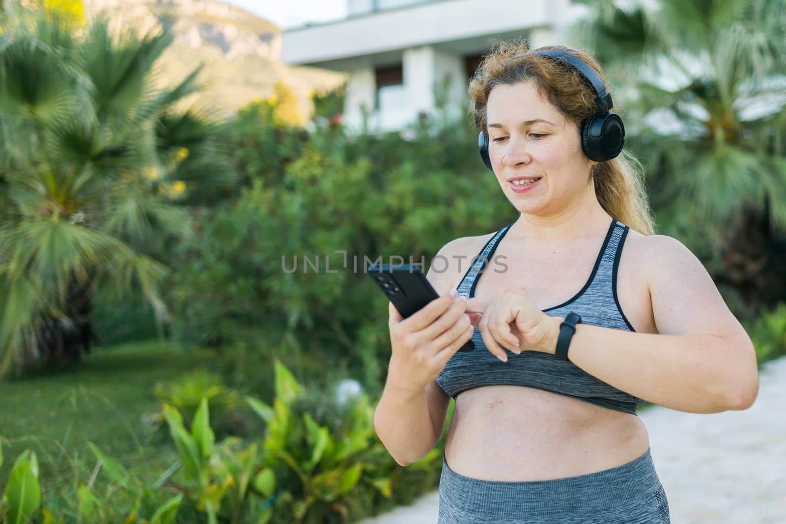 Fat woman checking time or heart rate from smart watch. Exercise or running outdoors for weight loss idea concept. Wellness and wellbeing copy space and empty space for text or advertising by Satura86