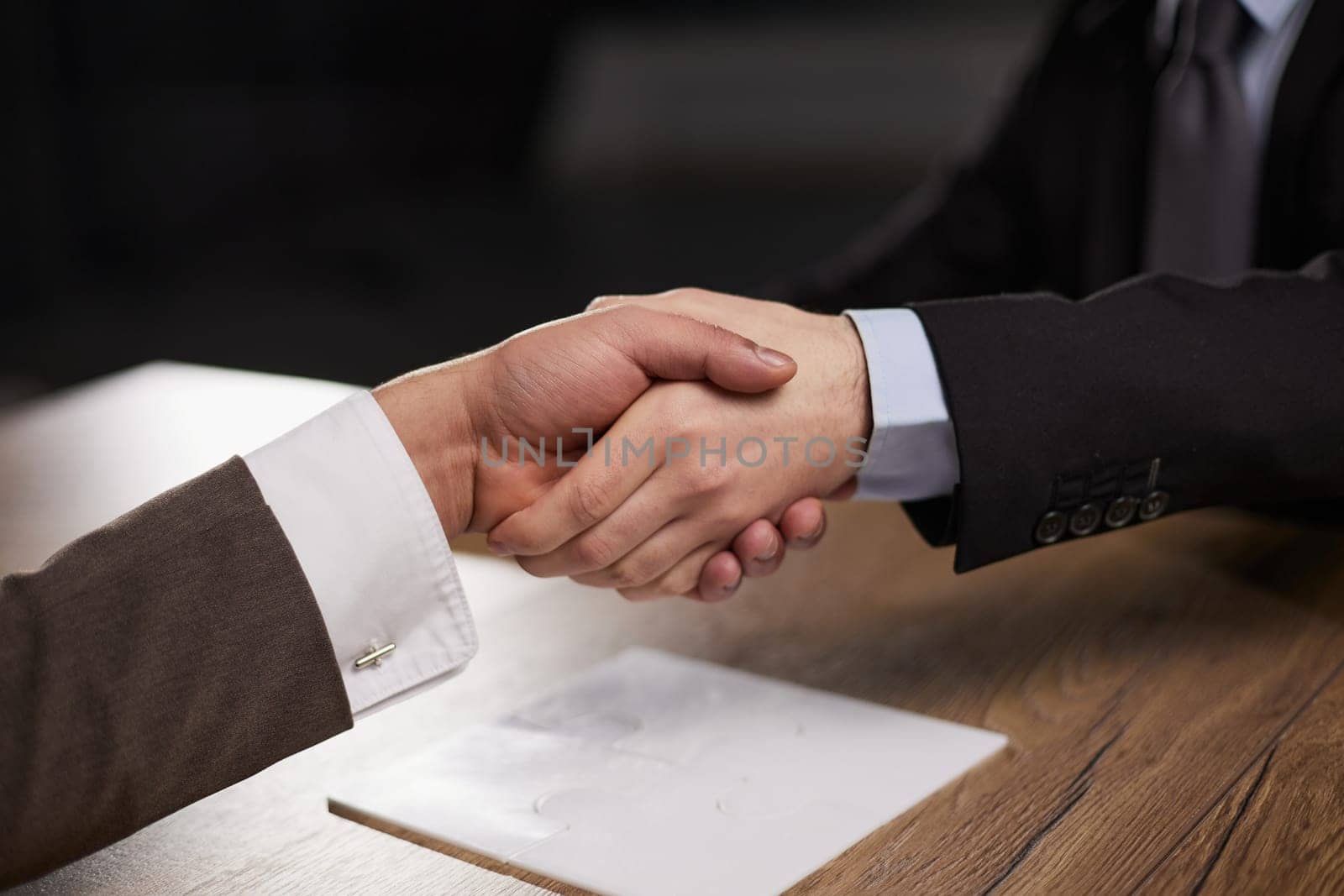 Closeup of hands of two young and successful male business people shaking hands over wooden table