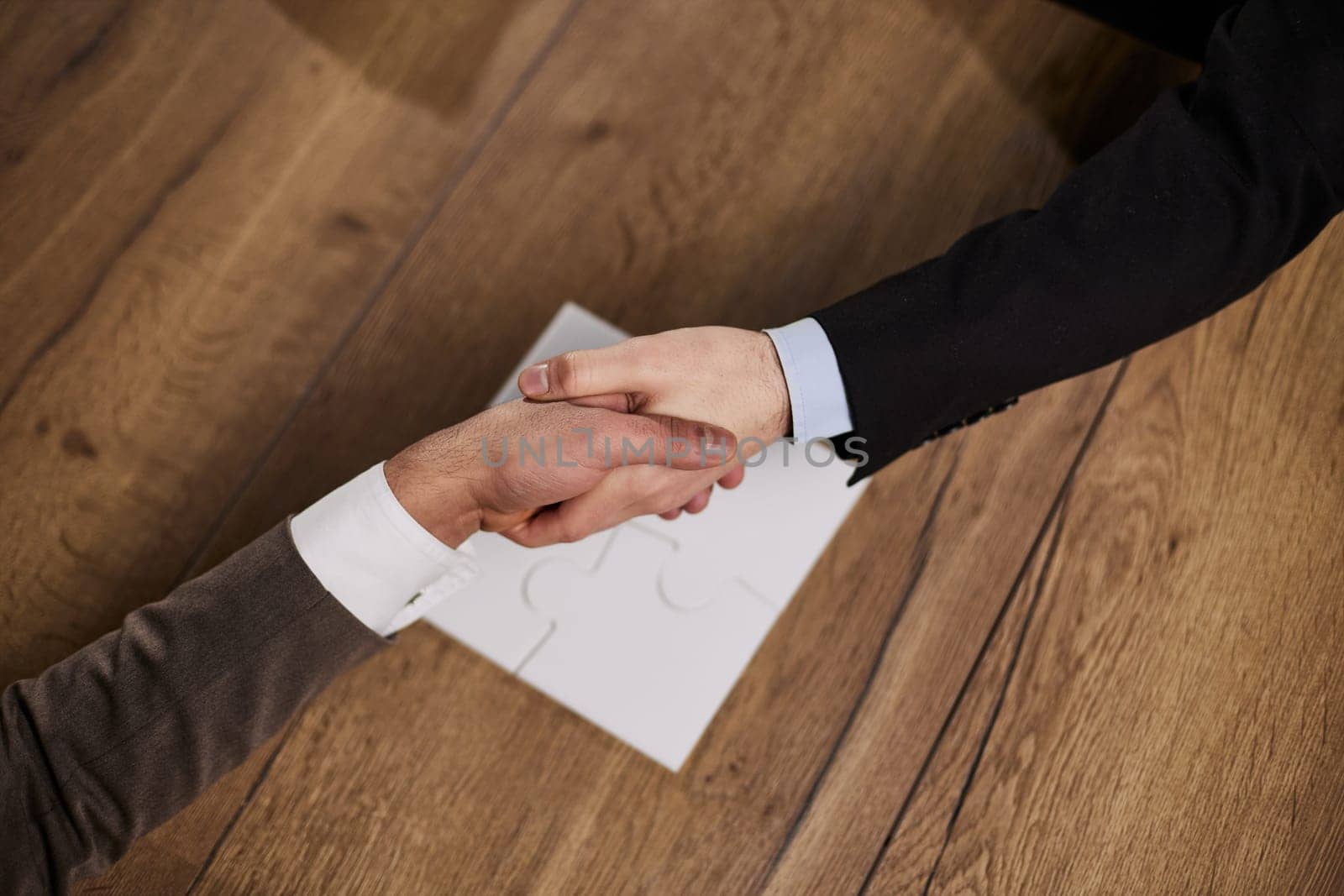 Closeup of hands of two young and successful male business people shaking hands over wooden table