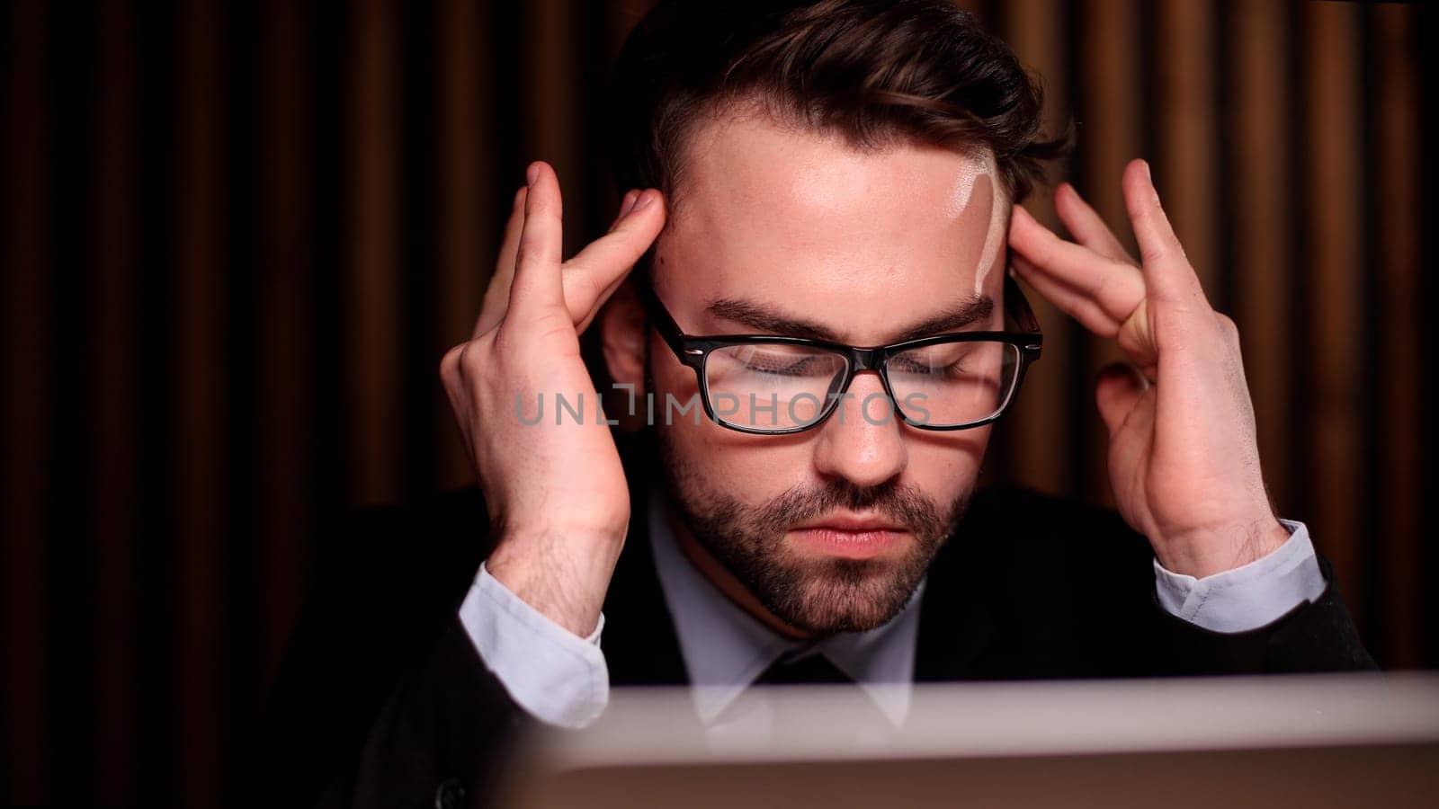 Tired exhausted man, office worker, manager or freelancer, sitting at his desk, tired of working in a laptop, overworked, having a headache, closed his eyes, needs rest and break