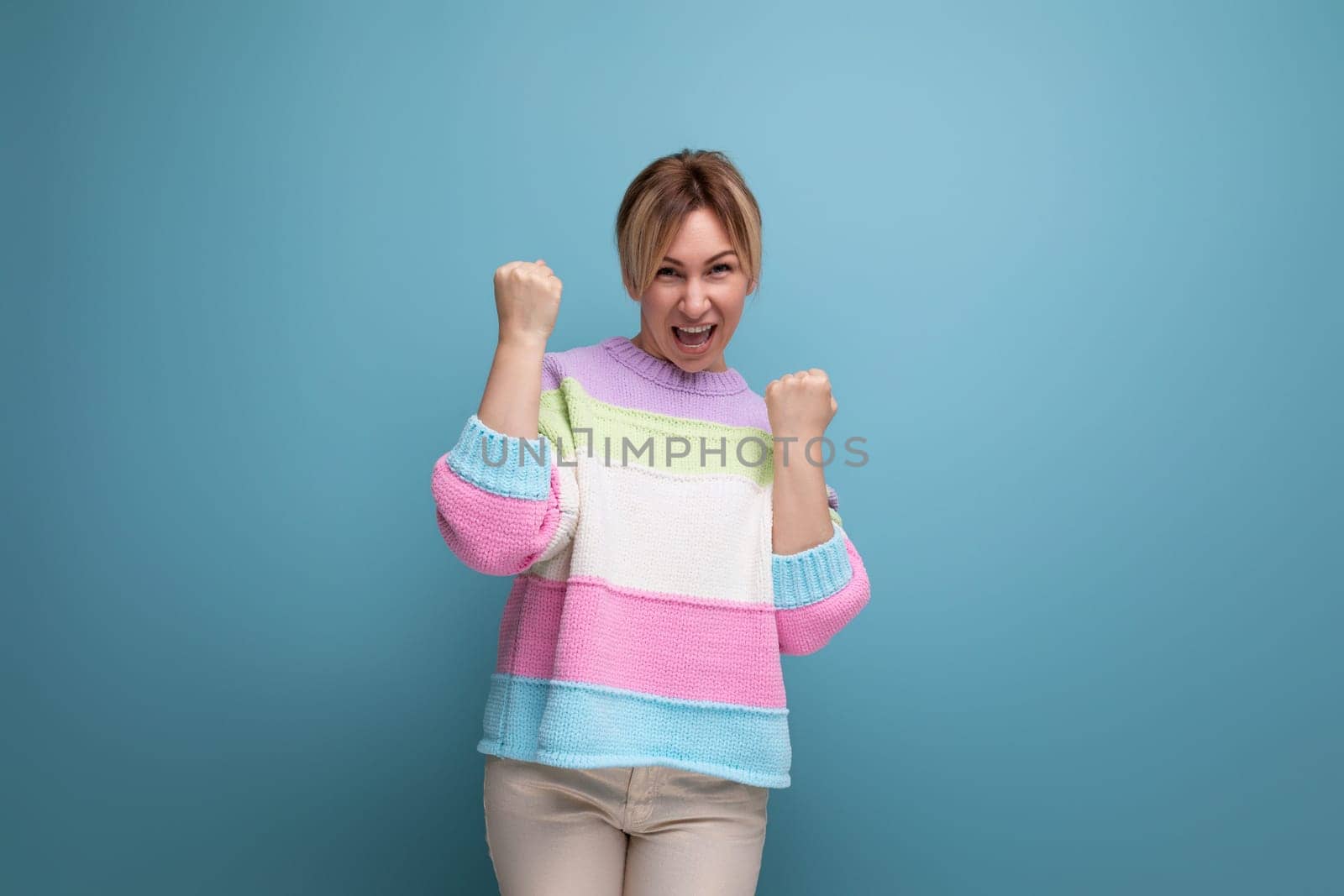 smiling blond woman in casual outfit rejoices in success on a blue background with copy space.