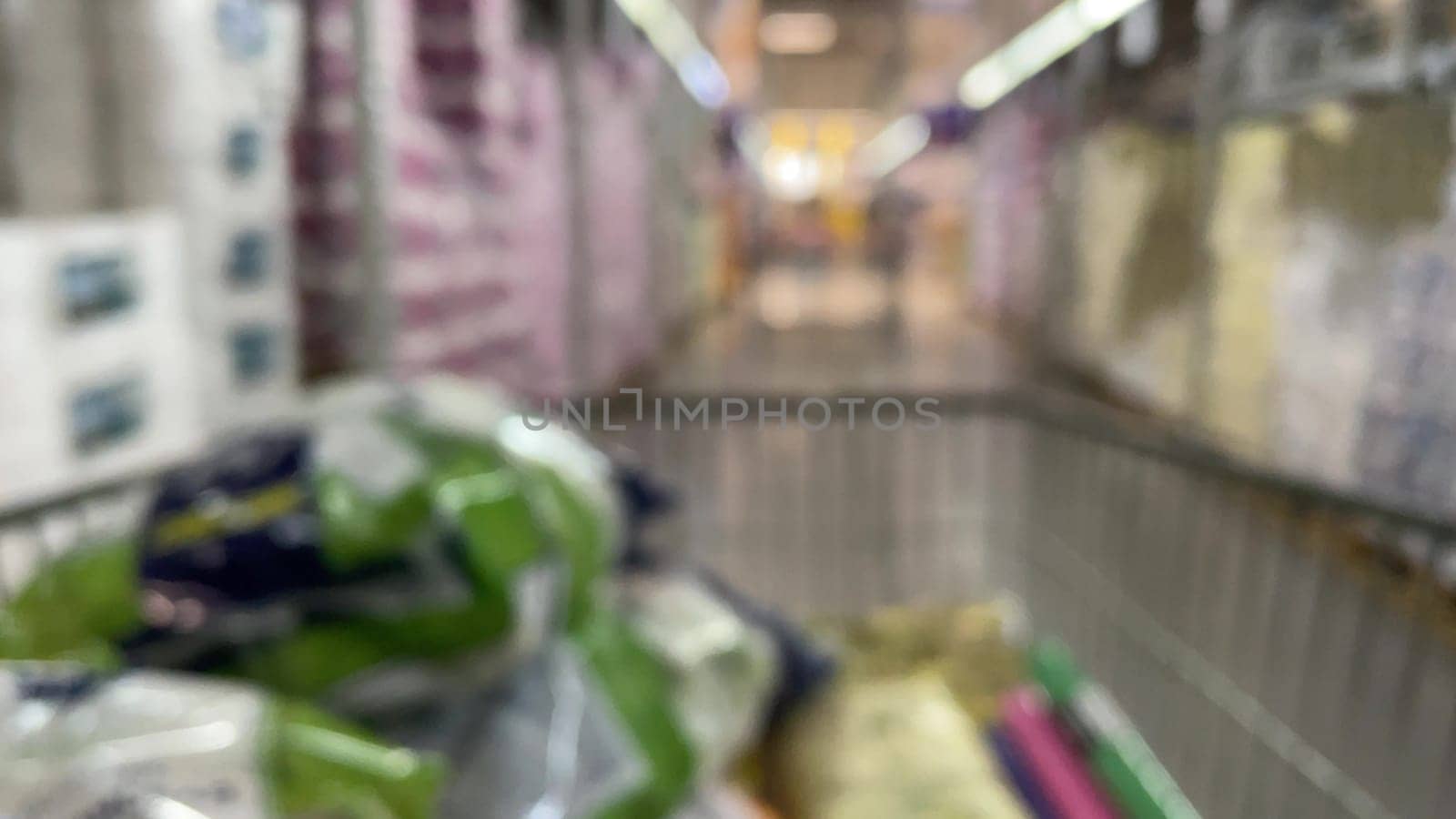 Trolley in a supermarket view from a shopping cart out of focus with unrecognizable people who choose products on a supermarket shelf. Buying food and essentials for the future