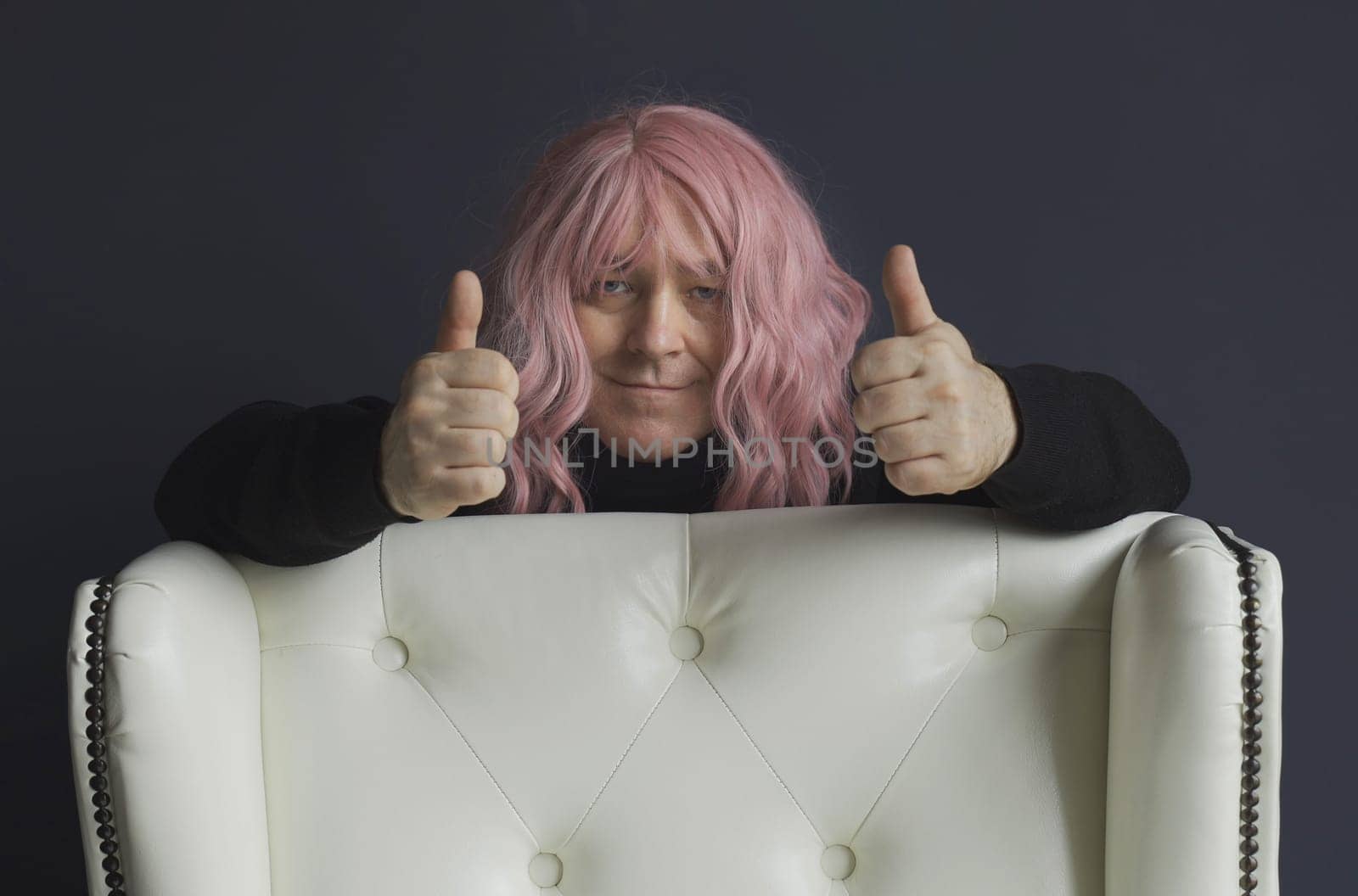 Positive man in a pink wig shows a gesture with his hands - thumbs up, great. Close-up.