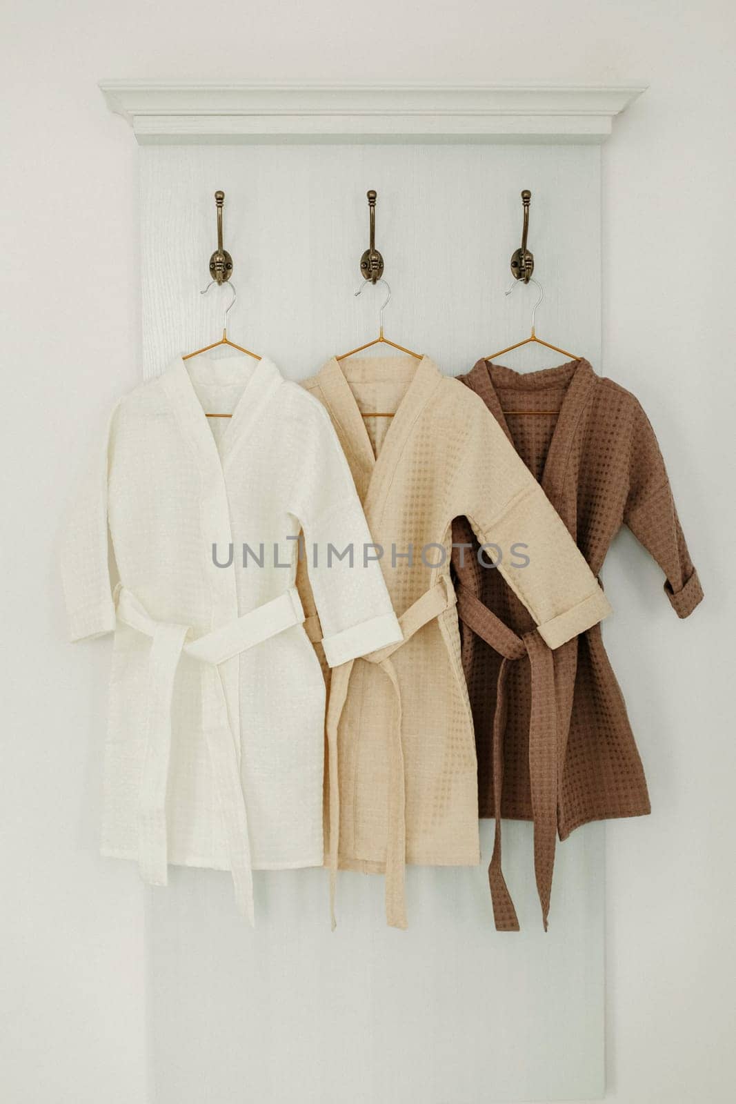Three linen robes of different colors hang on a hanger in the bathroom. Vertical frame.