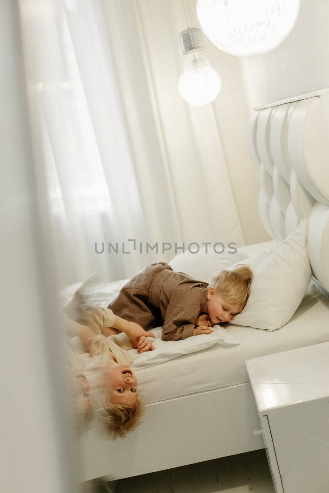 Boys, brothers lie on the bed in dressing gowns, play. The image is reflected in the mirror. Vertical frame.
