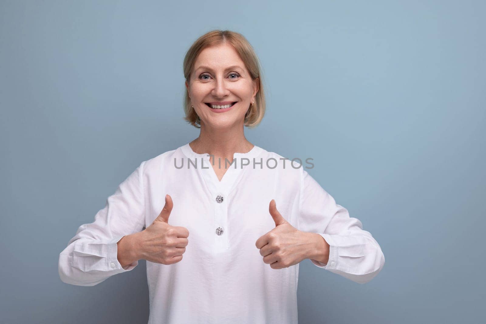 attractive blonde 50s woman in white blouse on studio background.