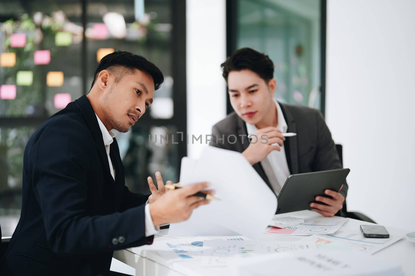 Two business men meeting to talking or discuss marketing work in workplace using paperwork, calculator, computer to work