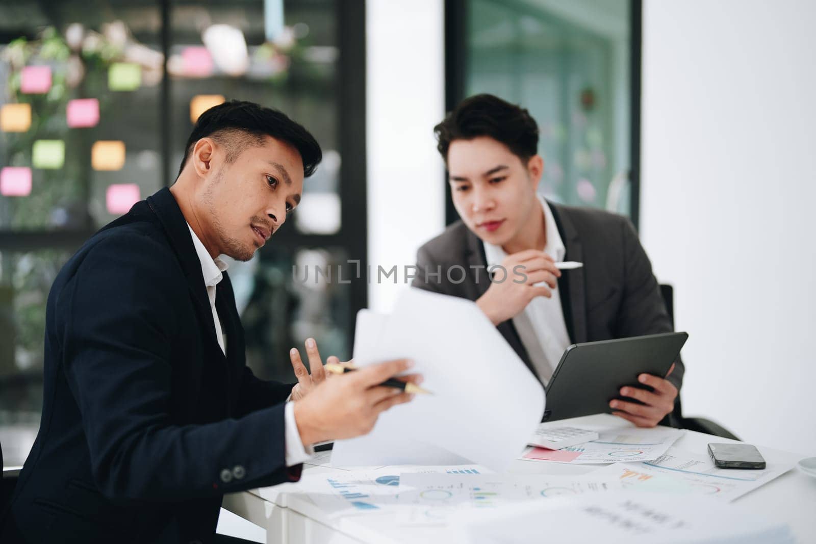 Two business men meeting to talking or discuss marketing work in workplace using paperwork, calculator, computer to work. by Manastrong