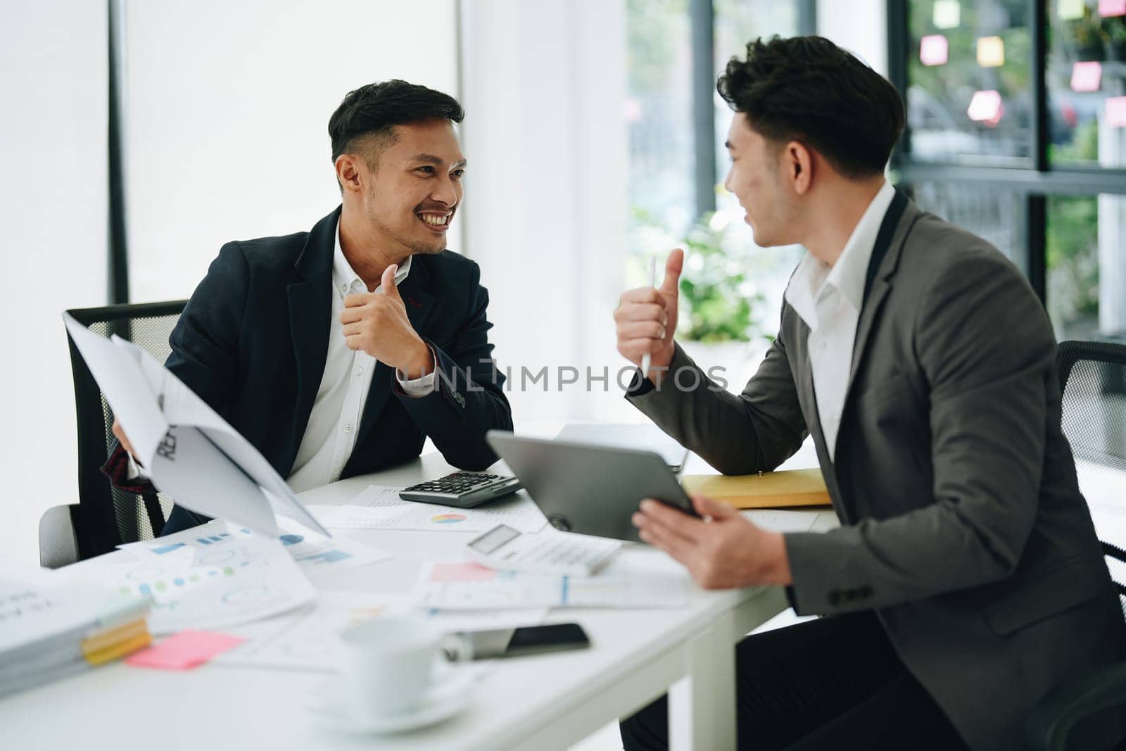 Two business men meeting to talking or discuss marketing work in workplace using paperwork, calculator, computer to work. by Manastrong