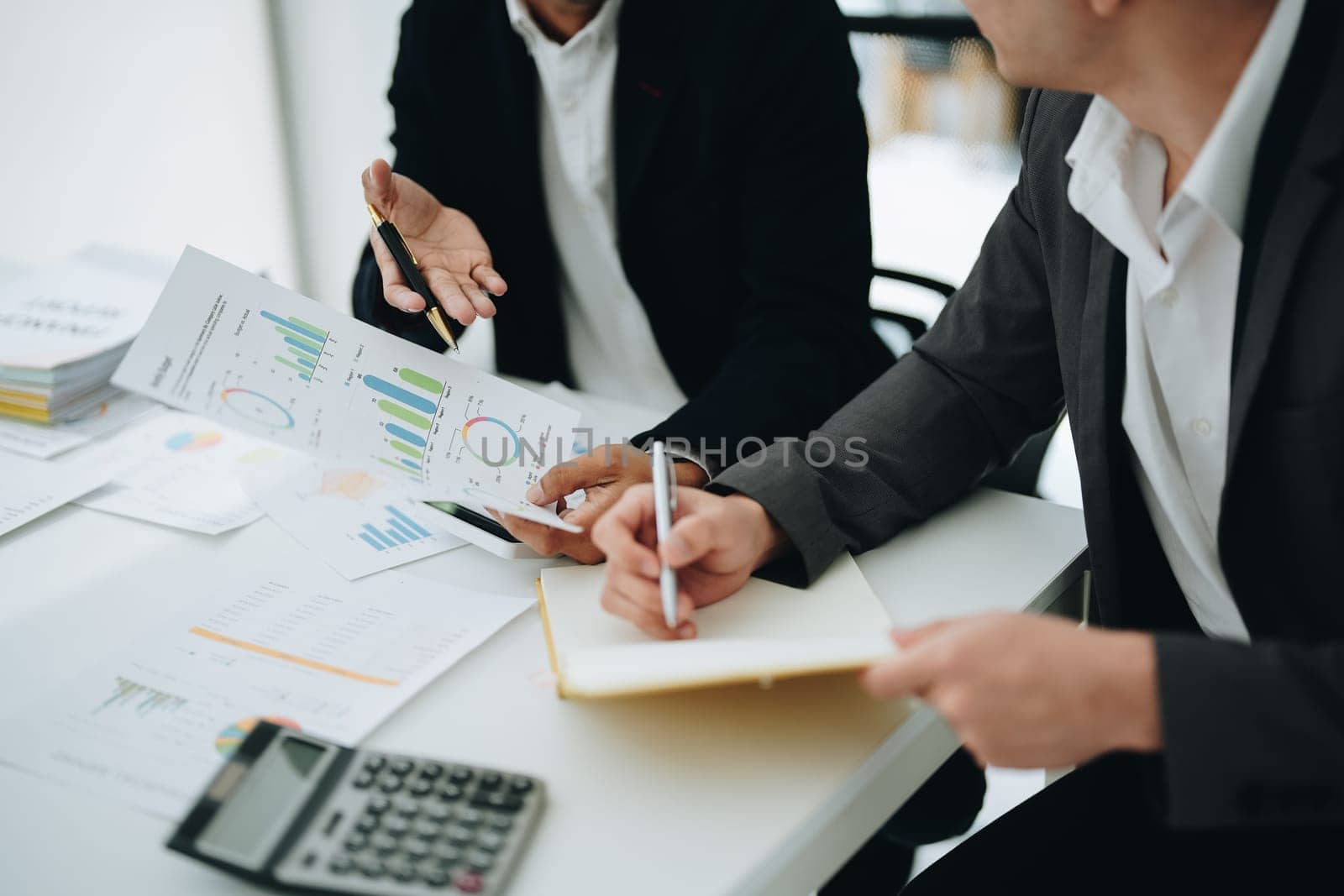 Two business men meeting to talking or discuss marketing work in workplace using paperwork, calculator, computer to work. by Manastrong