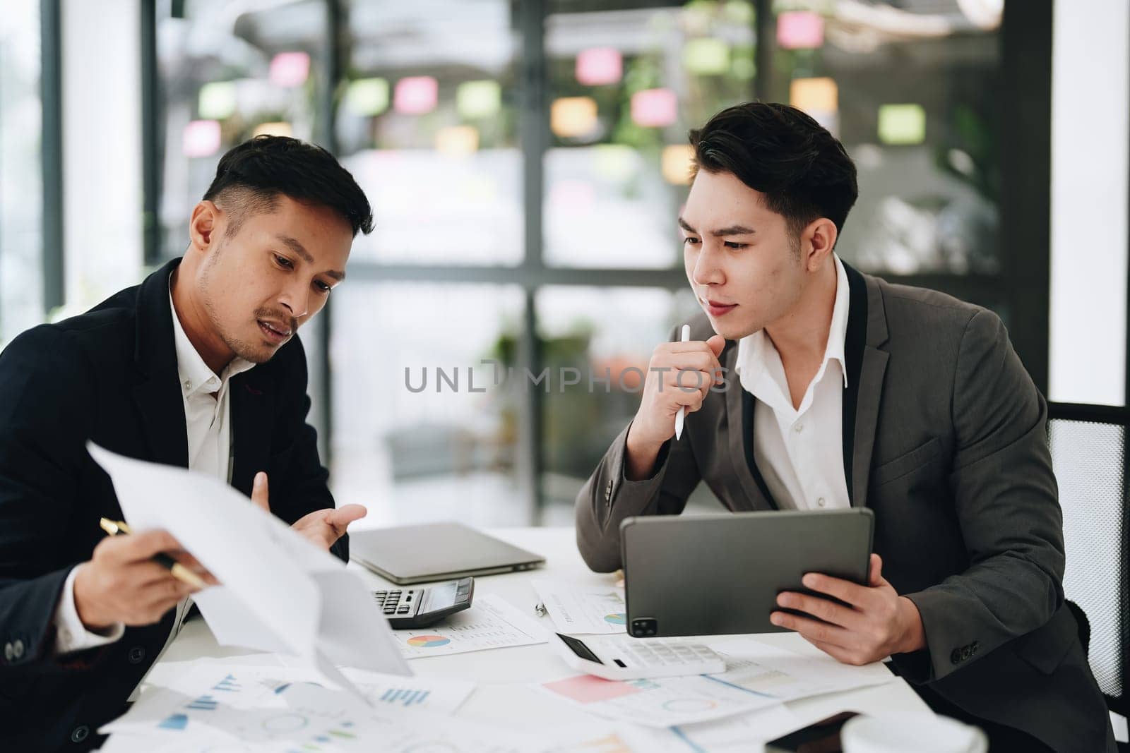 Two business men meeting to talking or discuss marketing work in workplace using paperwork, calculator, computer to work. by Manastrong