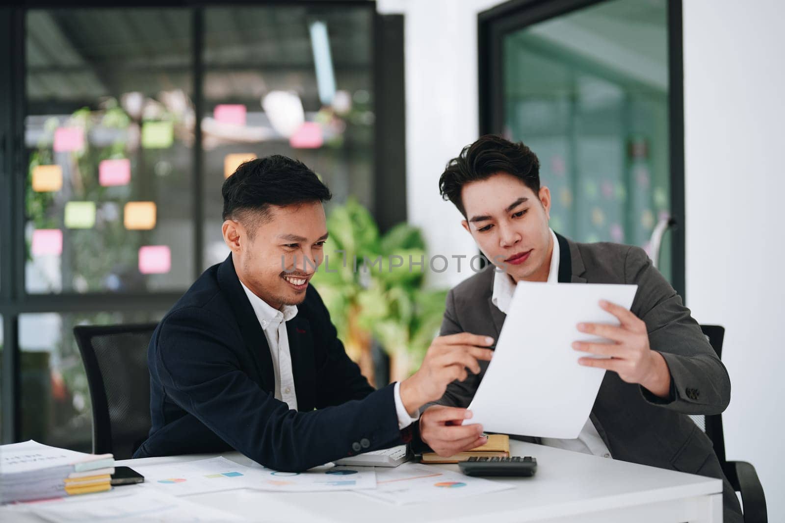 Two business men meeting to talking or discuss marketing work in workplace using paperwork, calculator, computer to work. by Manastrong