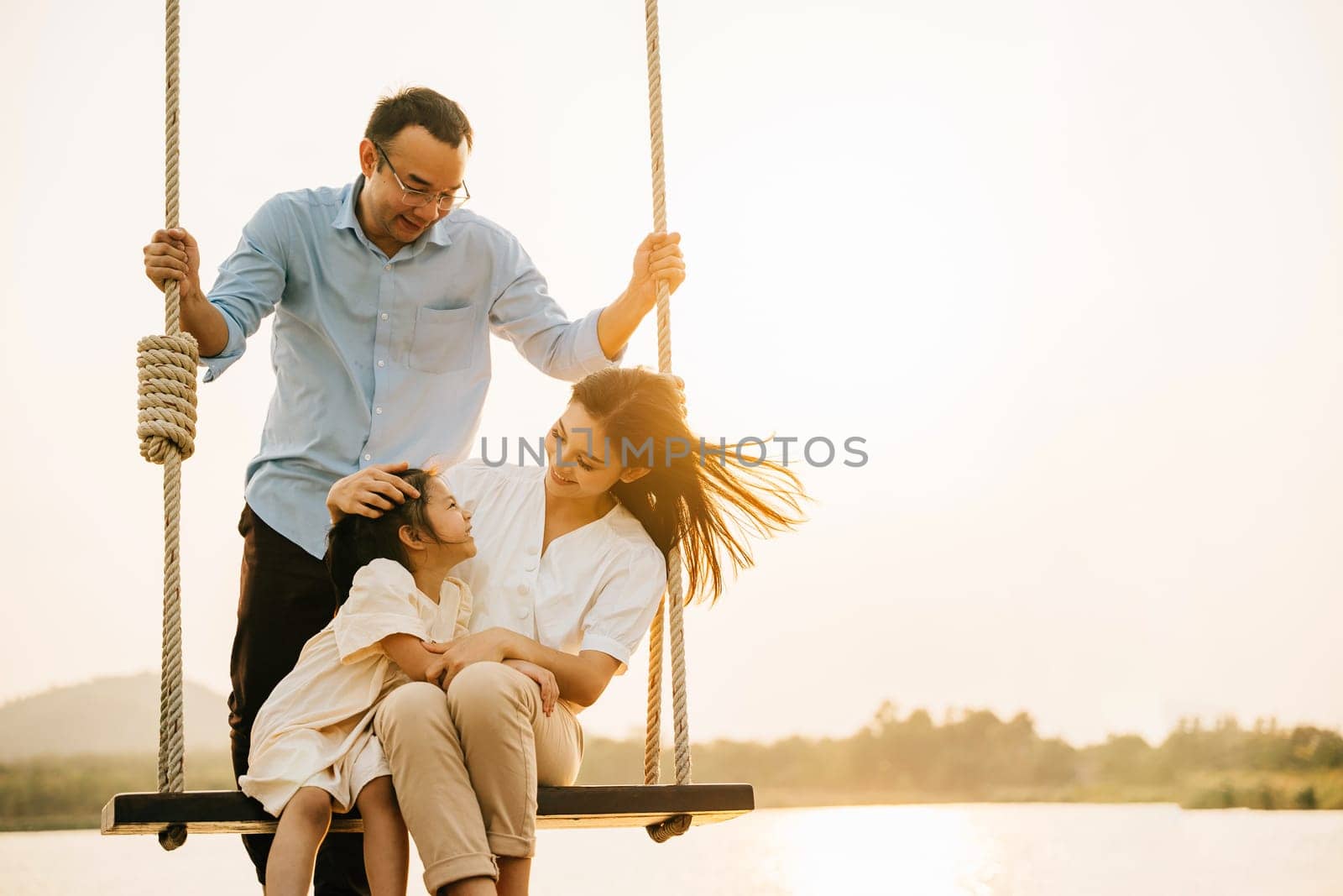 A happy family playing together on a swing set in a beautiful park, with the parents and children laughing and smiling in the sunshine, Happy Family Day