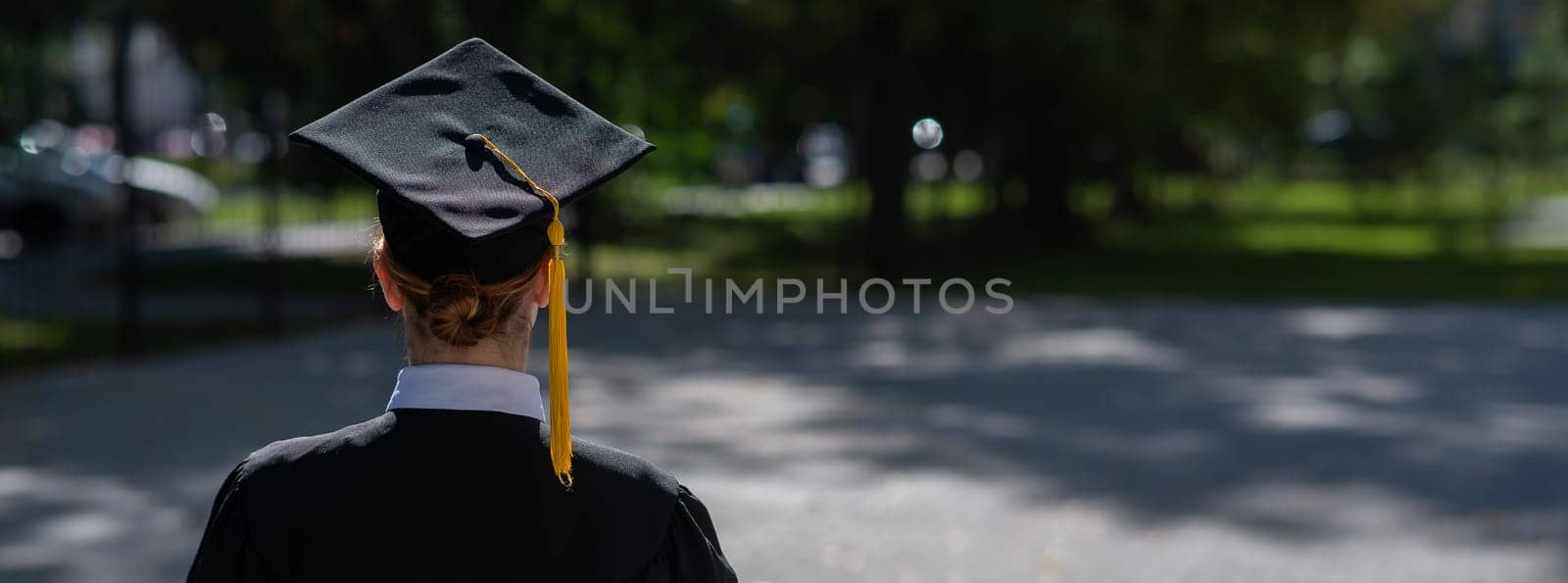 A woman throws her graduation cap against the blue sky. Widescreen. by mrwed54