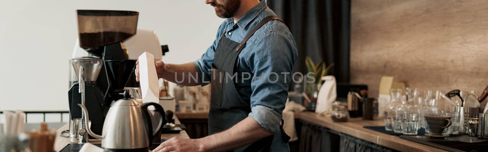 Barista pours coffee beans into the coffee machine tank for grinding standing behind counter