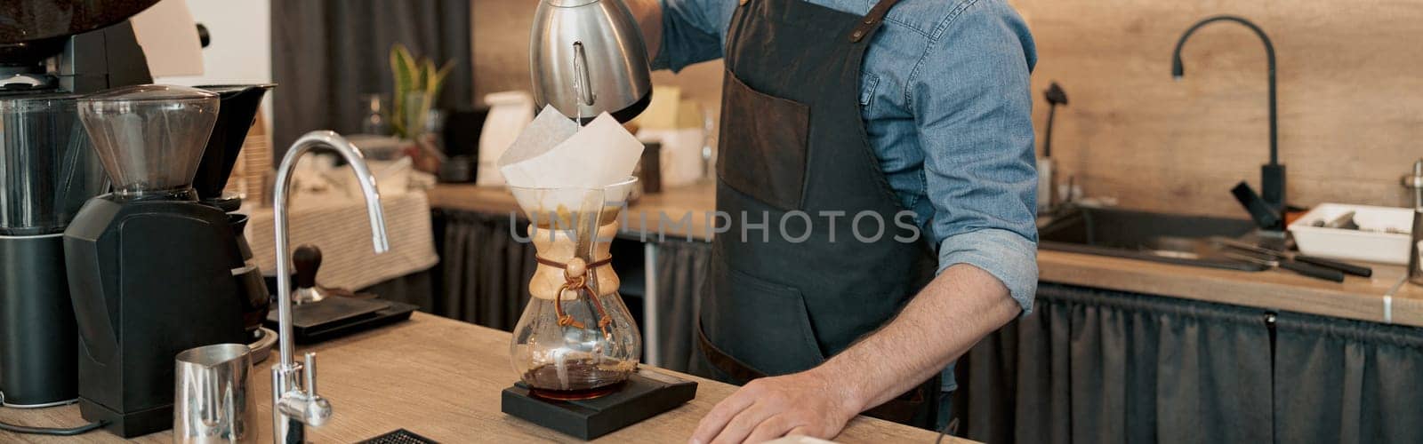 Barista with kettle in his hands pouring boiled water through filter into cup