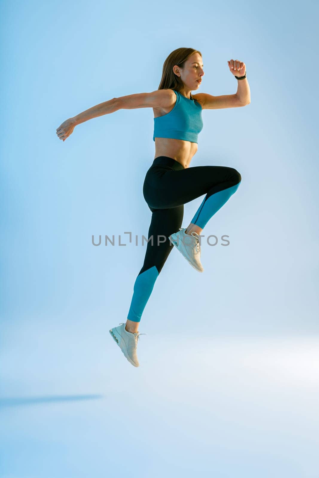 Athletic active fitness woman jumping on studio background . Dynamic movement by Yaroslav_astakhov