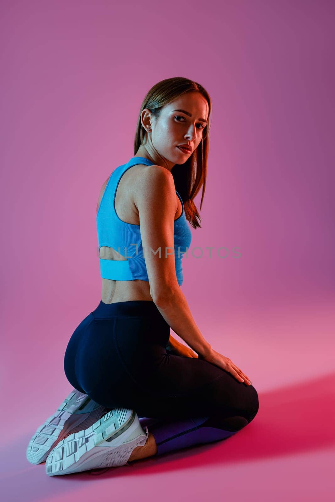 Athletic woman wearing sportswear is kneeling and posing on studio background. High quality photo