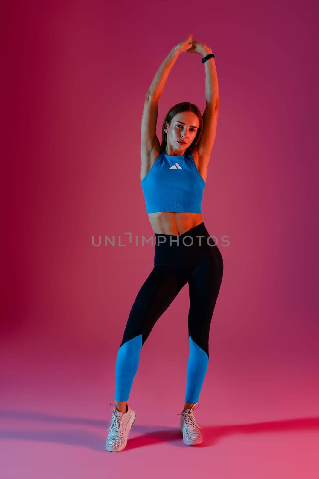 Young active woman wearing sportswear posing with hands raised up on studio background by Yaroslav_astakhov