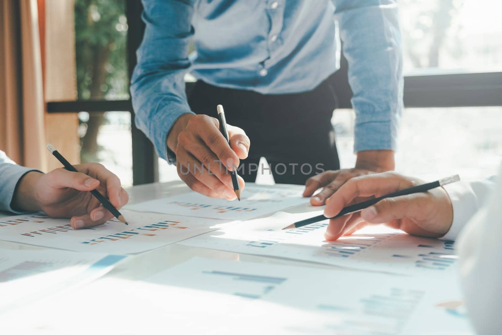 Close-up of businessmen working together at workplace, discussing about strategies, plans, analytic progress, and financial stats, and pointing at graph documents on desk holding pencils. Business and Teamwork concept.