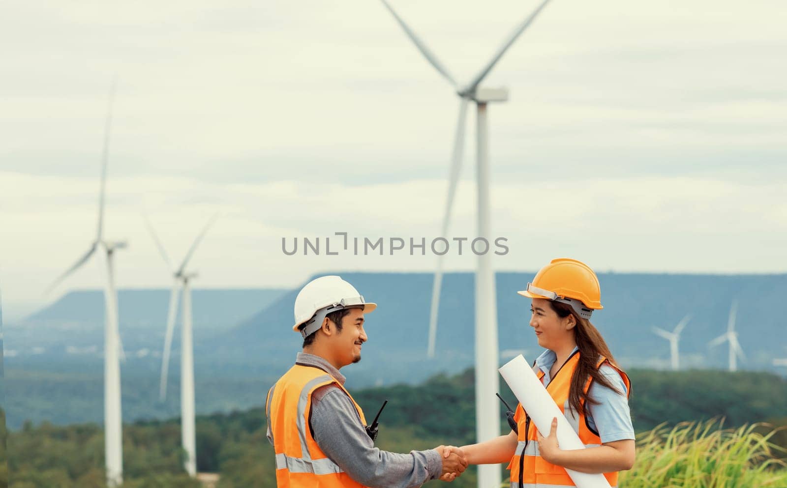 Male and female engineers working on a wind farm atop a hill or mountain in the rural. Progressive ideal for the future production of renewable, sustainable energy.