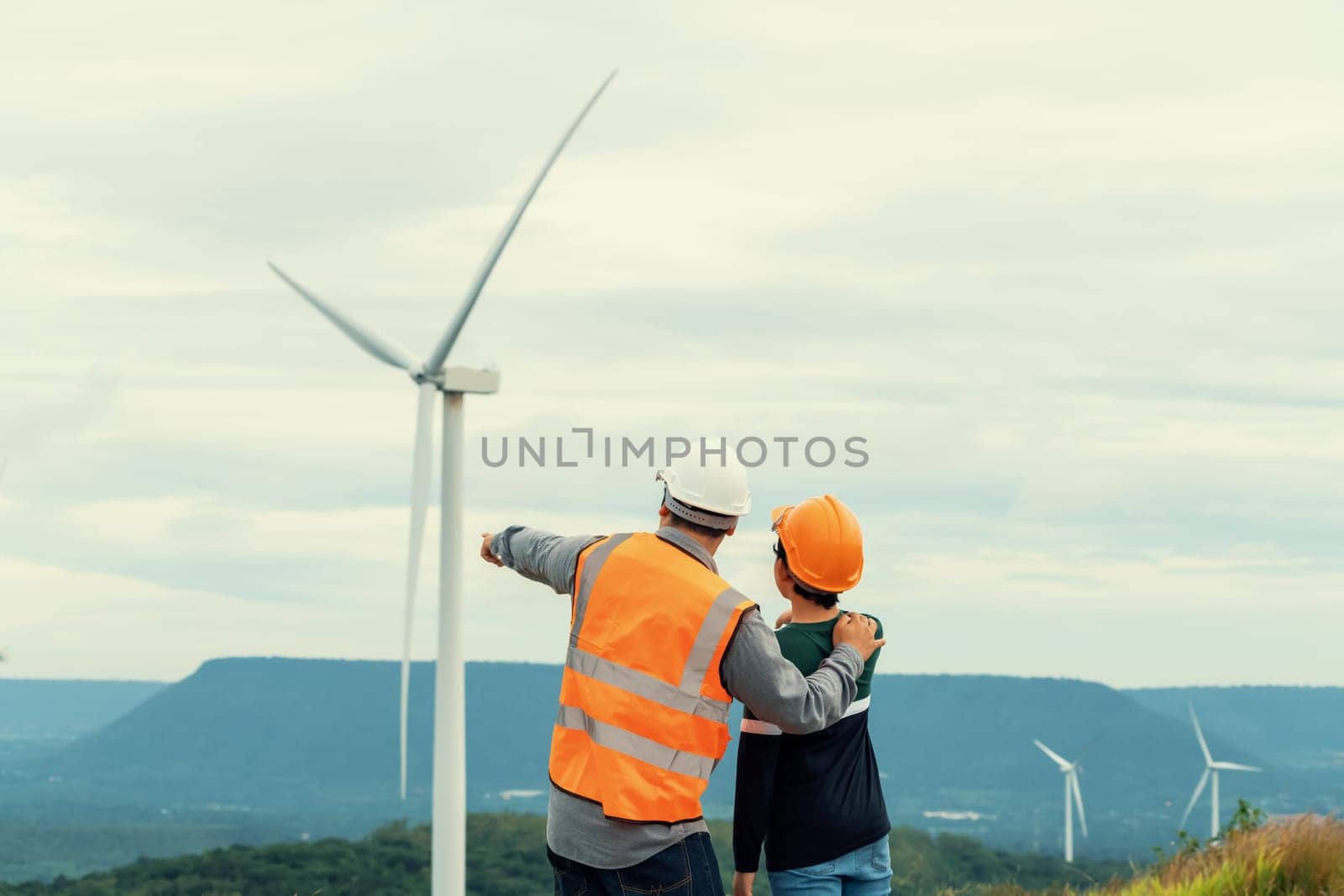 Engineer with his son on a wind farm atop a hill or mountain in the rural. Progressive ideal for the future production of renewable, sustainable energy. Energy generation from wind turbine.