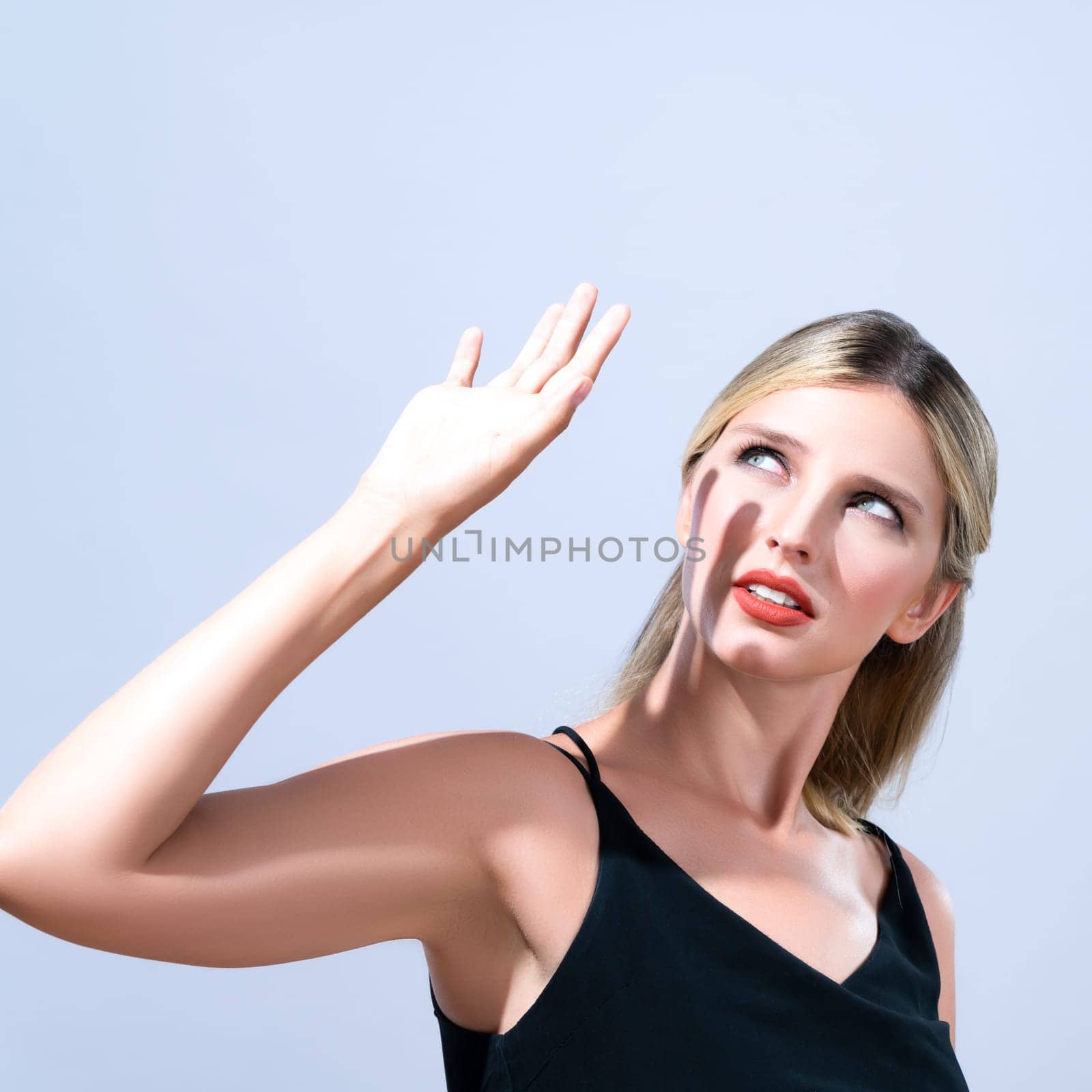 Closeup young blond hair woman with perfect skin and soft alluring facial makeup raise her hand cover her face from bright sunlight in isolated background for skincare sunscreen product.