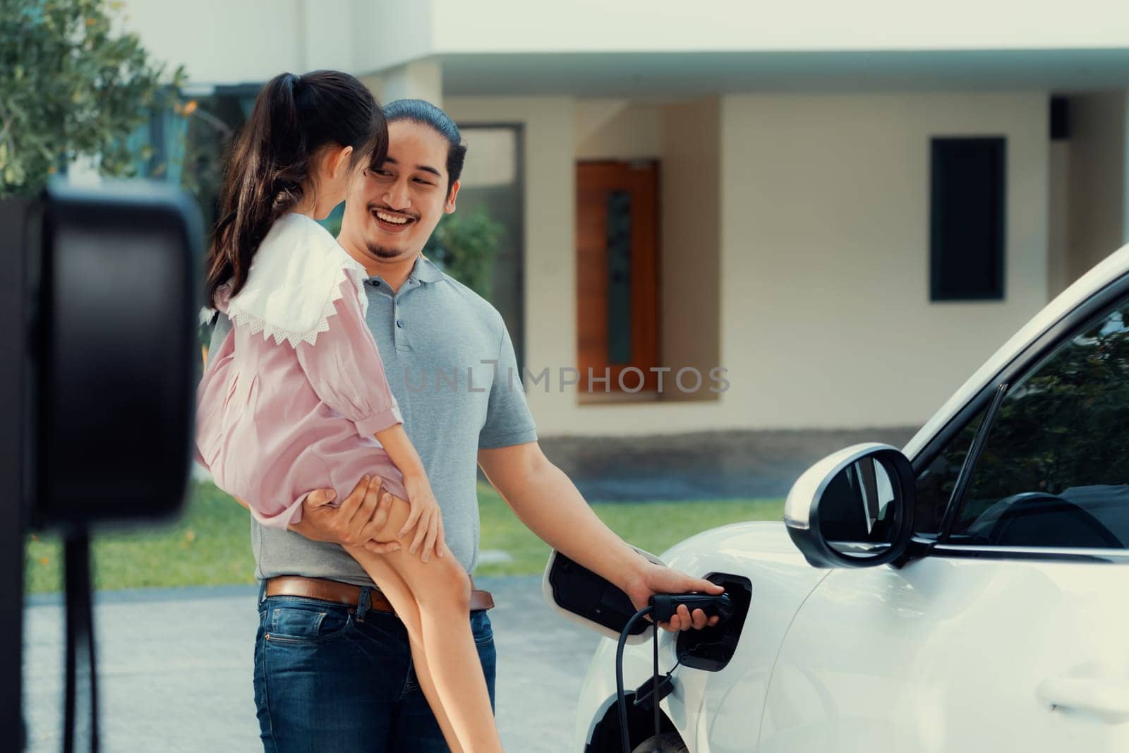 Progressive concept of father and daughter with EV car and home charging station by biancoblue