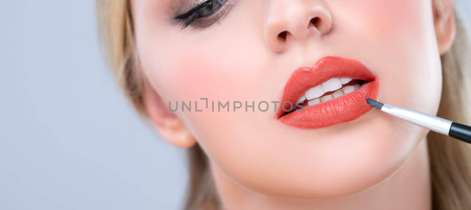 Closeup beautiful young woman putting alluring fashion glossy red lipstick. by biancoblue