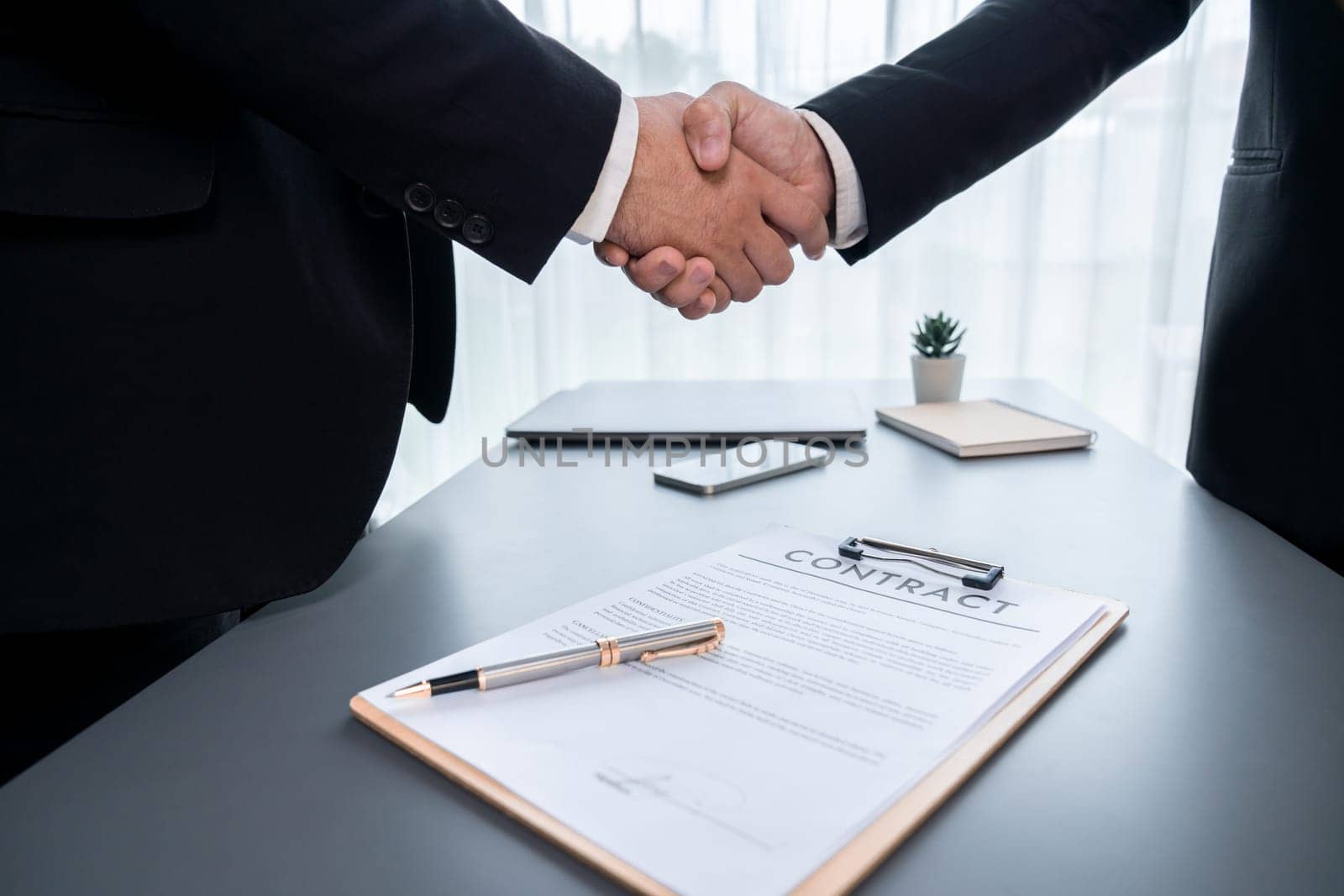 Two professionals successfully close business deal with closeup handshake, sealing the partnership agreement. Legal document and handshaking as formal agreement between two companies. Fervent