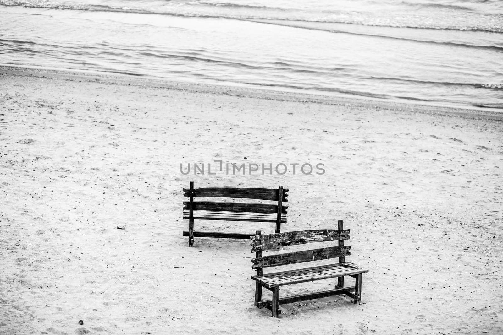 Two wooden benches stand on the beach with sand. by AnatoliiFoto