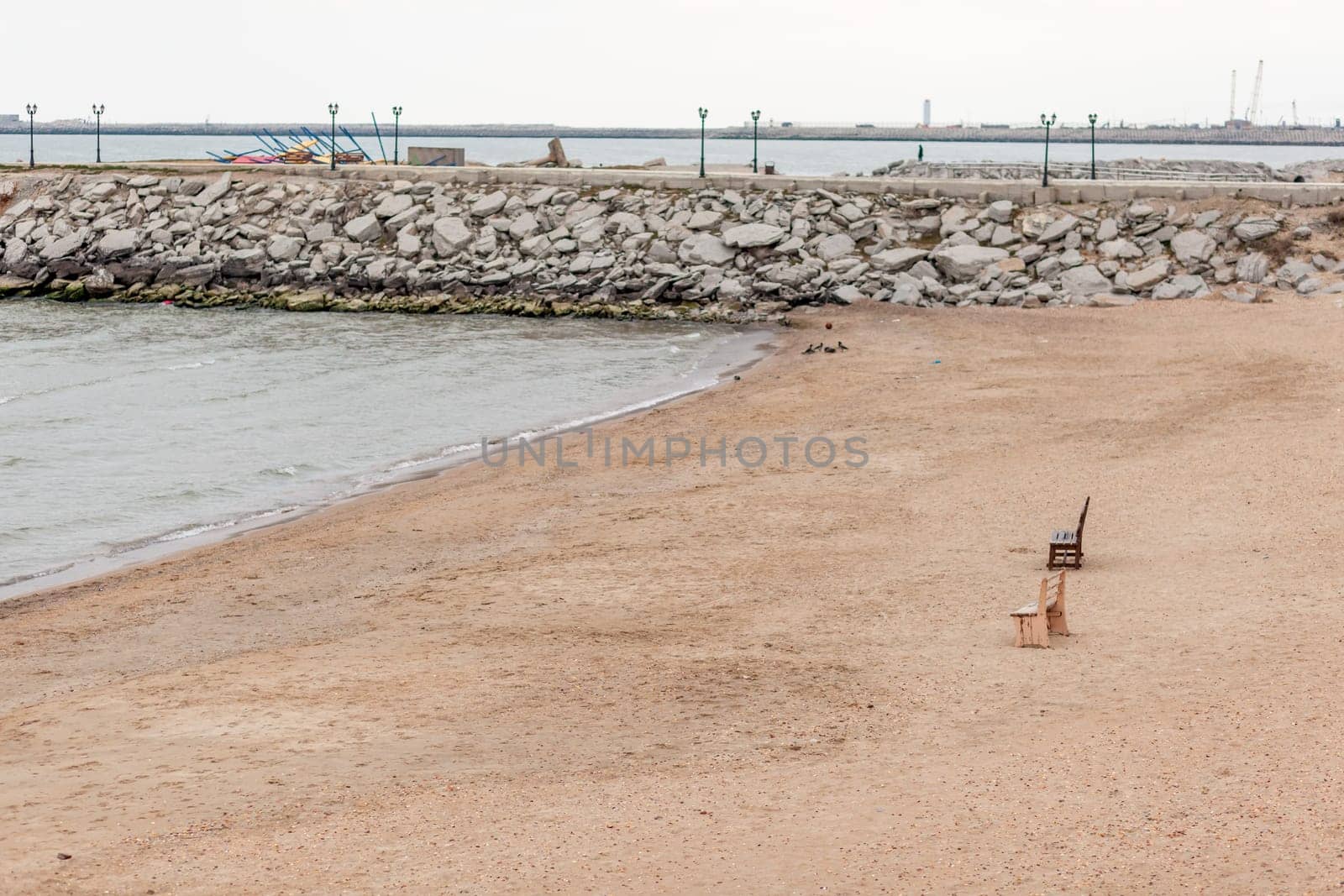 Two wooden benches stand on the beach with sand. by AnatoliiFoto