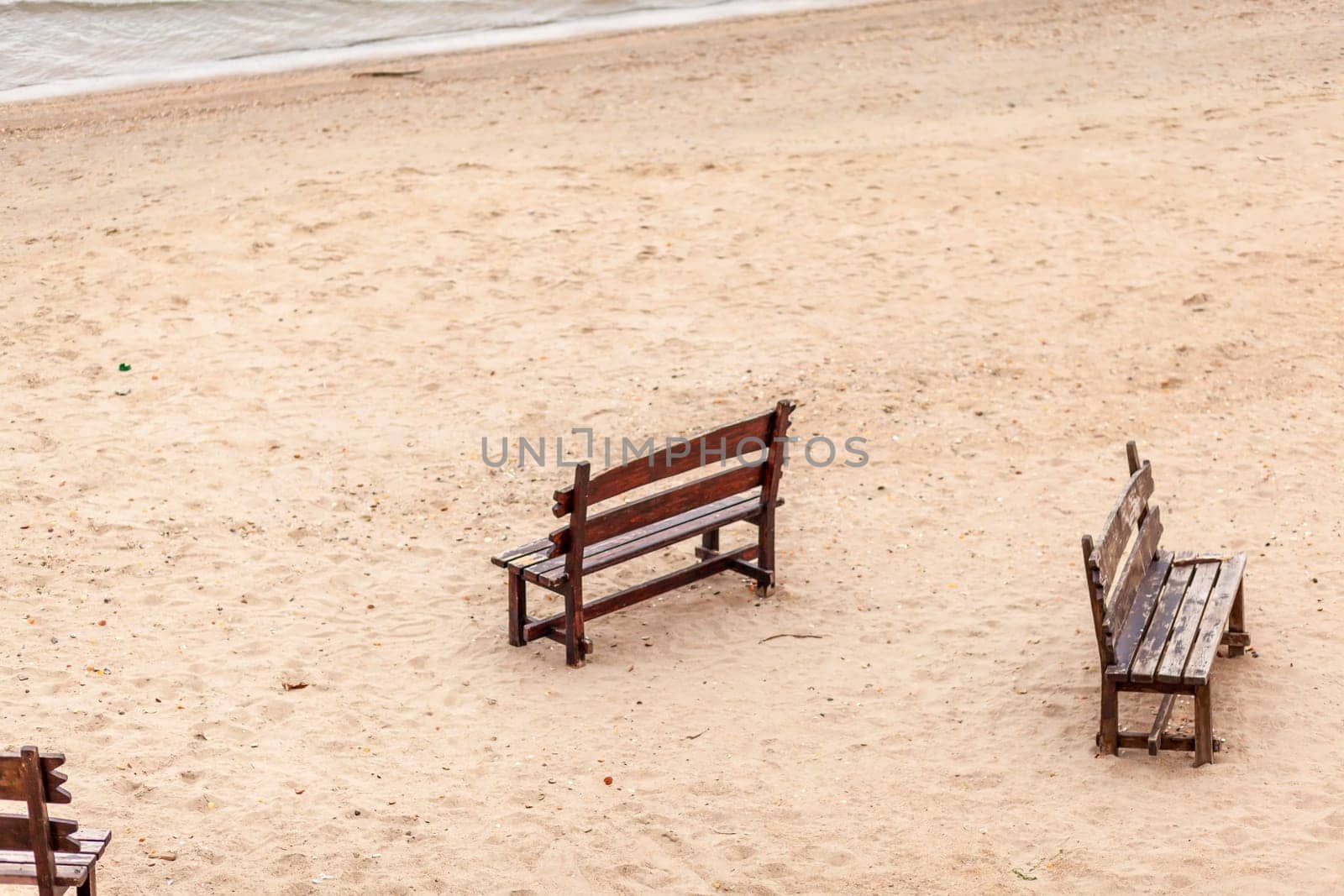 Two wooden benches stand on the beach with sand. by AnatoliiFoto