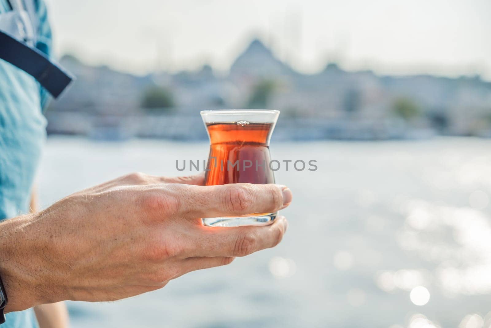 Man in Istanbul having breakfast with Simit and a glass of Turkish tea. Glass of Turkish tea and bagel Simit against golden horn bay in Istanbul, Turkey. Turkiye.