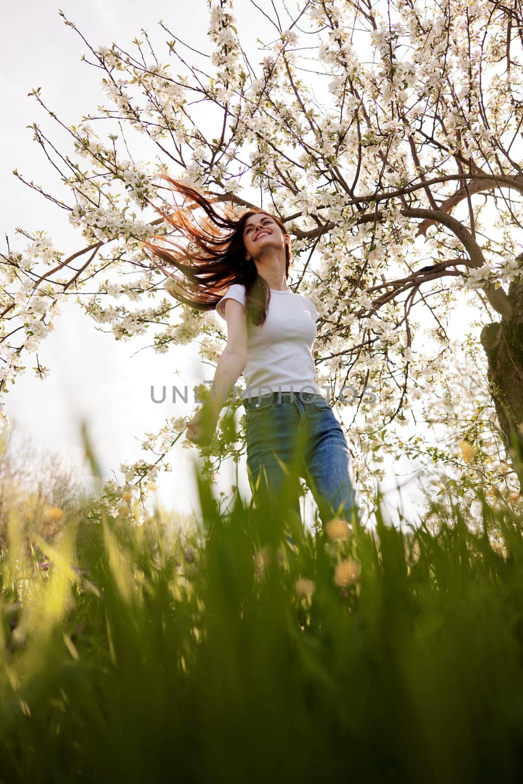 joyful woman stands against the background of a flowering tree in summer clothes by Vichizh