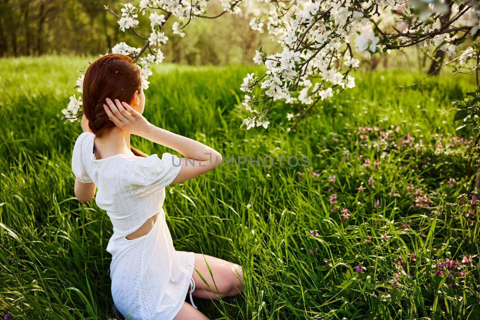 a woman in a light dress sits with her back to the camera near a flowering apple tree by Vichizh