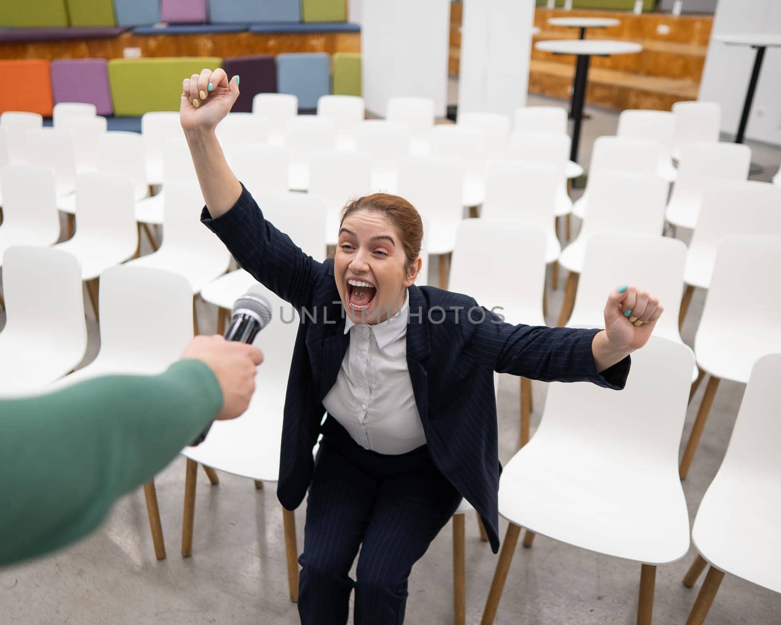 A red-haired Caucasian business woman sits in the front row in an empty conference room and answers into an outstretched microphone