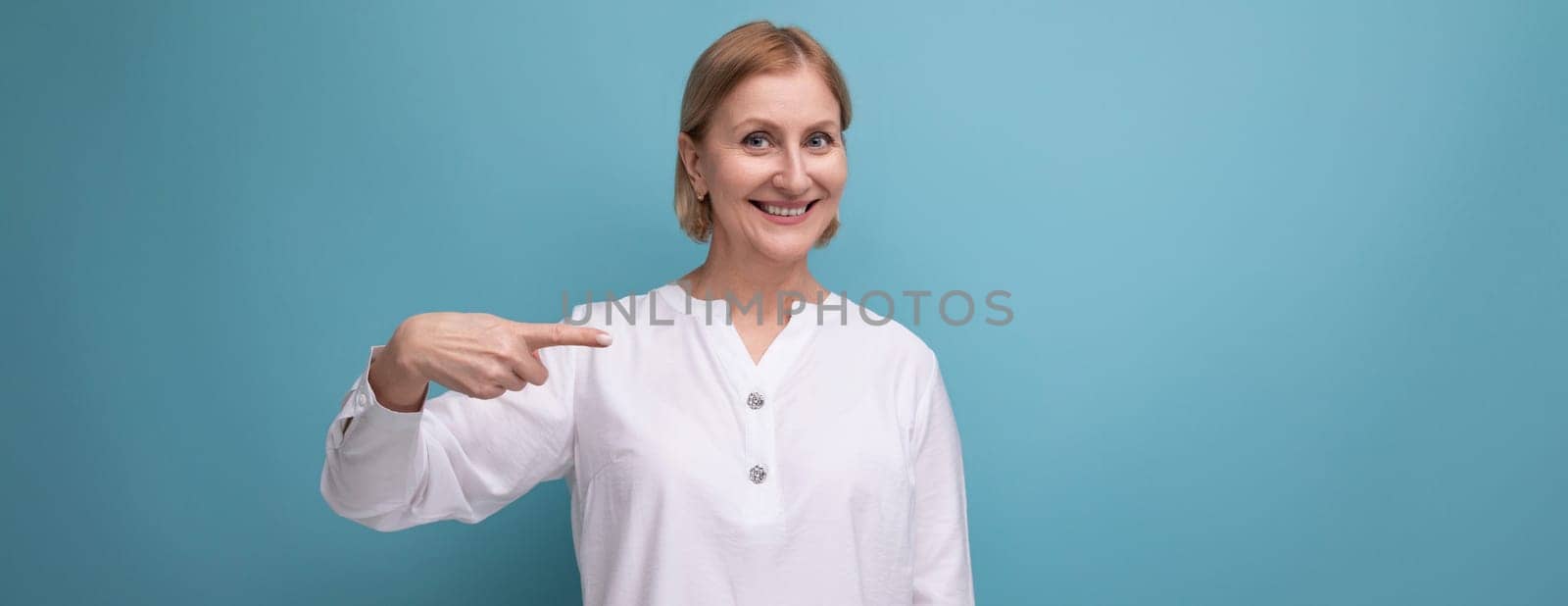 well-groomed blonde middle-aged woman in a white blouse on a studio background with copyspace by TRMK