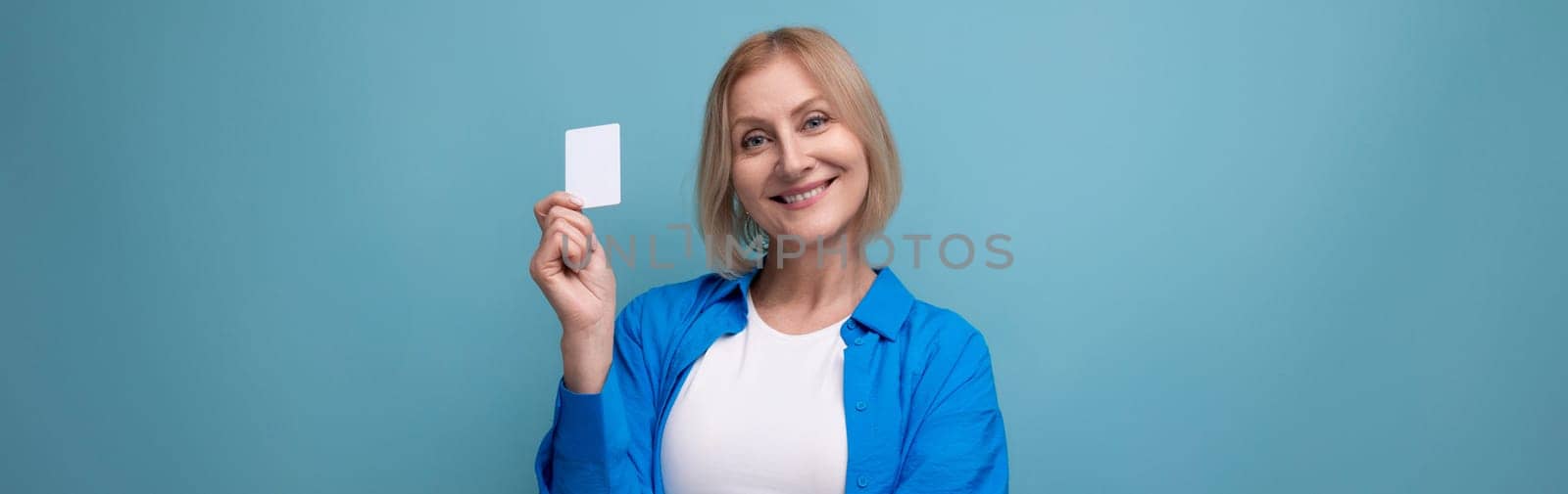 blonde middle-aged woman with a bob haircut holding a credit card on a studio background.