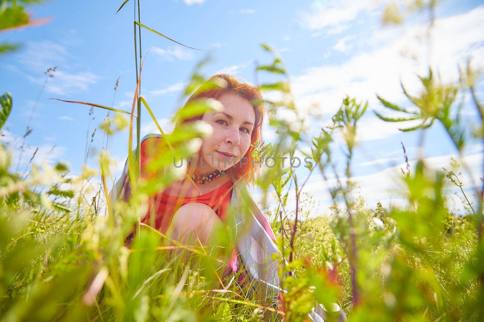 Outdoors portrait of red haired woman in grass and lower on a field and meadow. Young woman enjoying her freedom in flowering nature by keleny