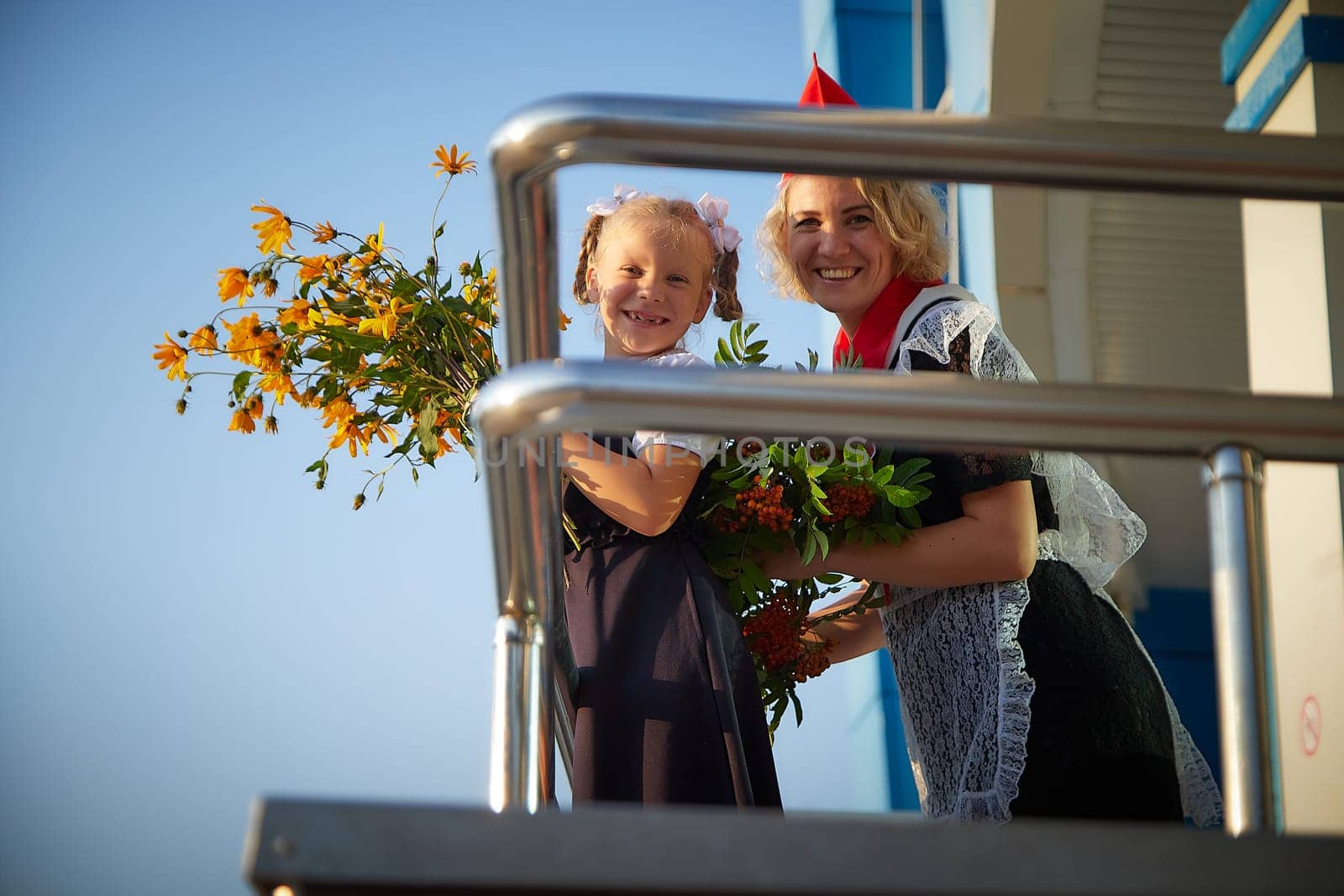 Young and adult schoolgirl on September 1 with flowers. Generations of schoolchildren of USSR and Russia. Female pioneer in red tie and October girl in modern uniform. Mother and daughter having fun by keleny