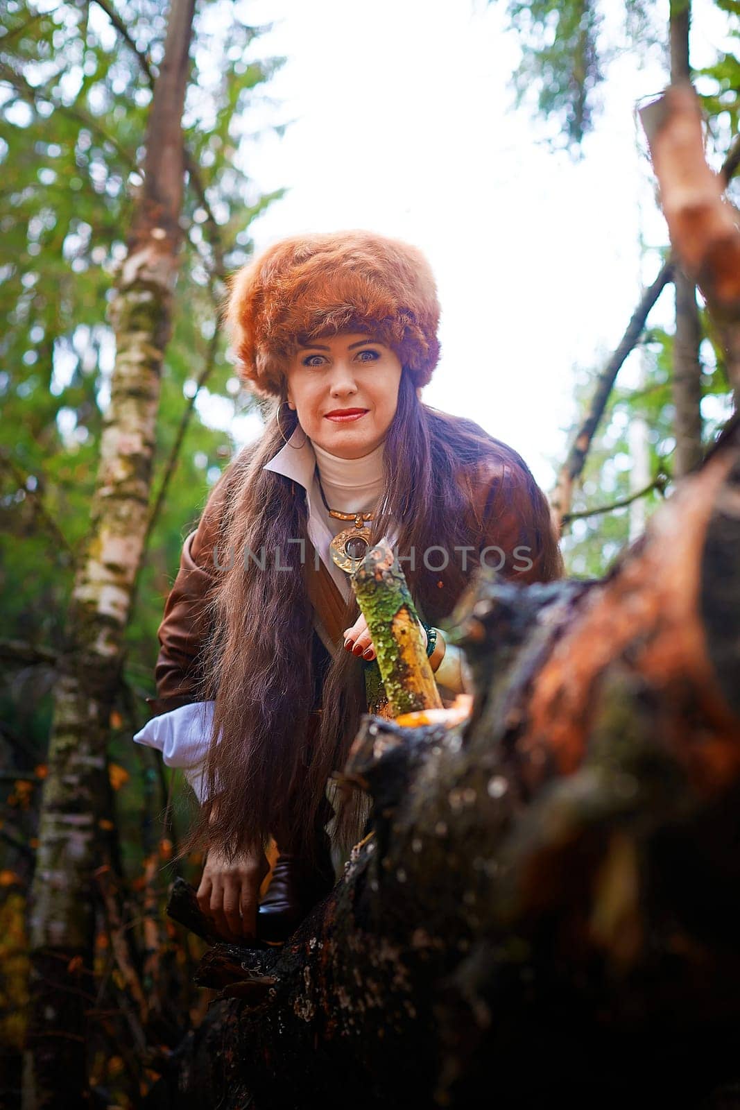 Girl in a leather jacket, a big red fox fur hat in the forest in autumn. A female model poses as a fabulous royal huntress on nature hunt at photo shoot by keleny