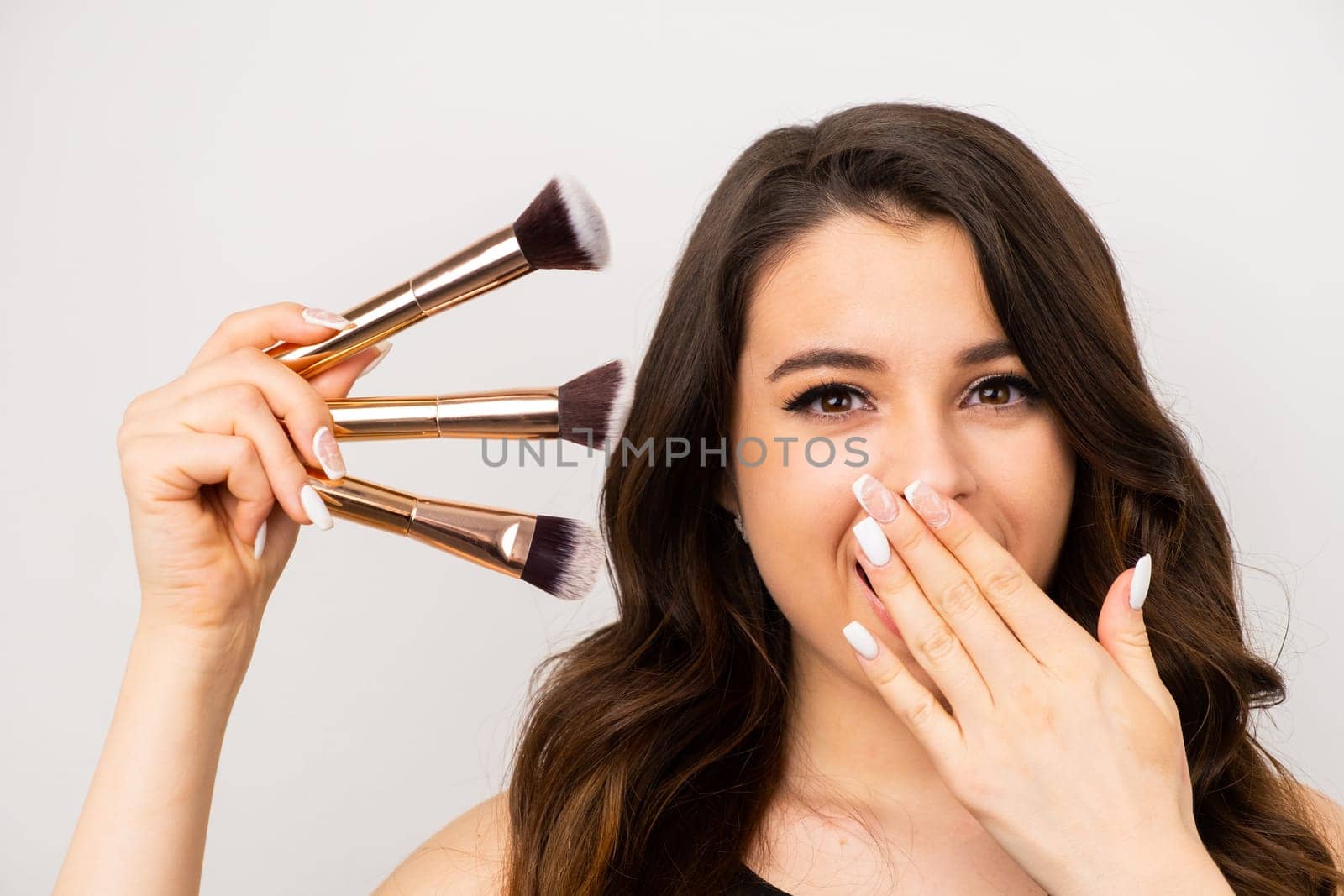 An exciting model with cosmetic brushes on a grey background. Makeup artist with professional tools.